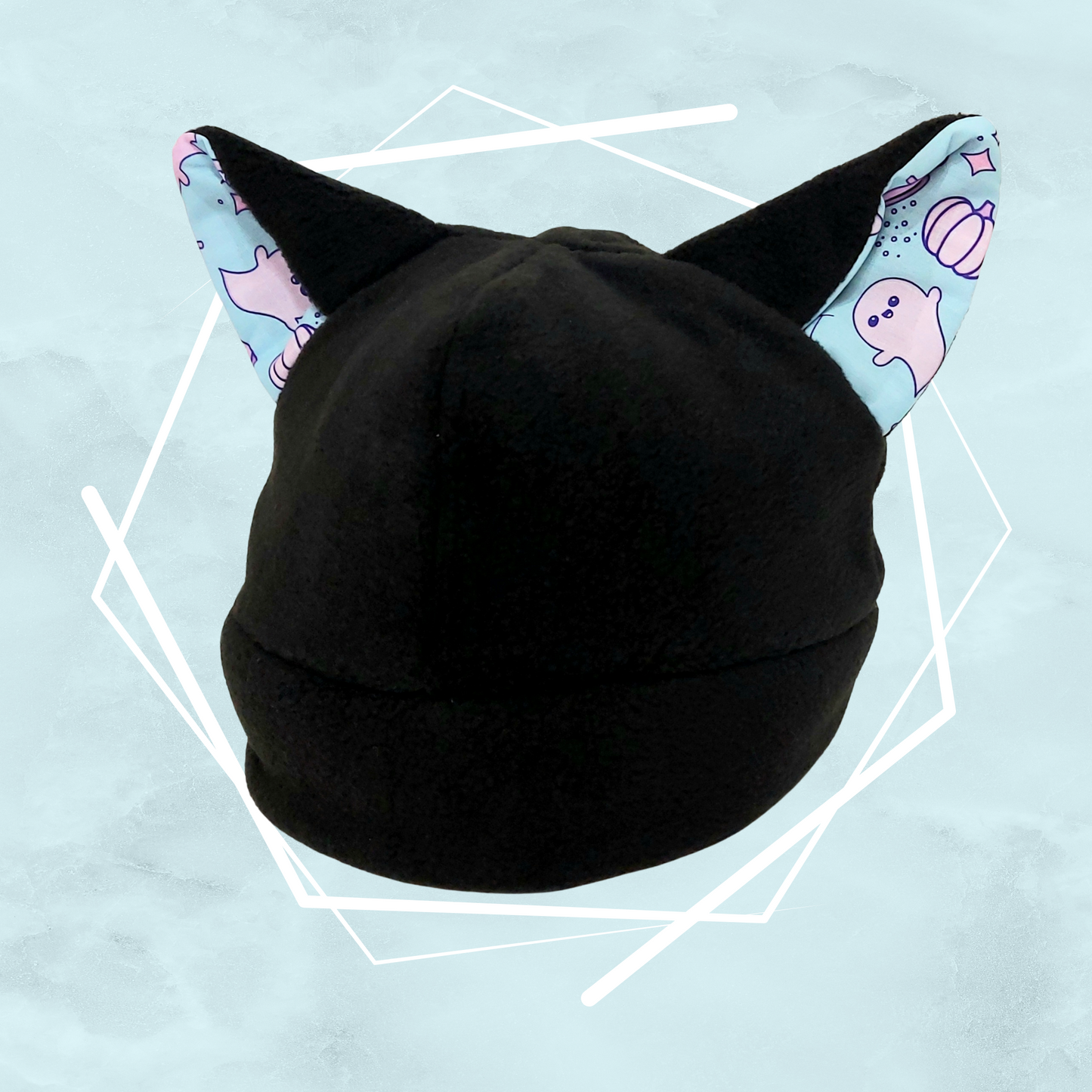 A handcrafted black nekomimi beanie with cat ears featuring a quirky pattern with cute ghost-like figures on a blue background.