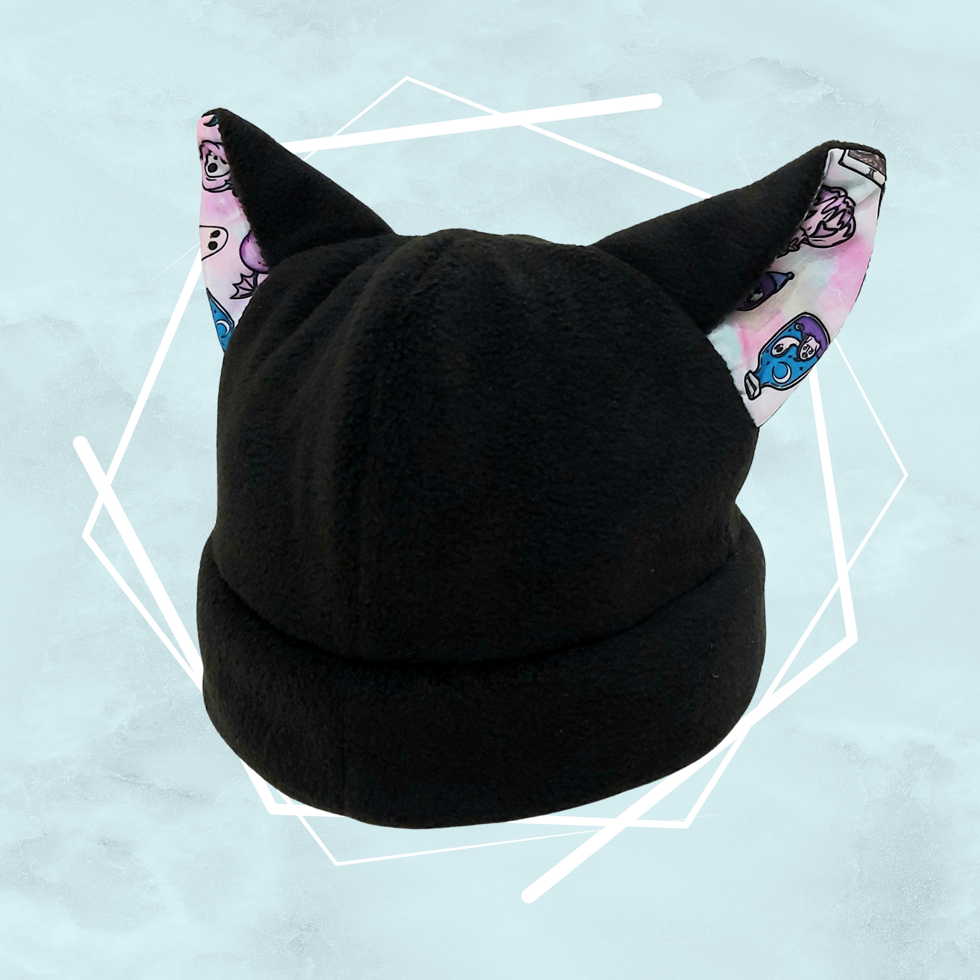 A black beanie with nekomimi cat ears featuring a colorful pattern with pink witchy Halloween-themed illustrations