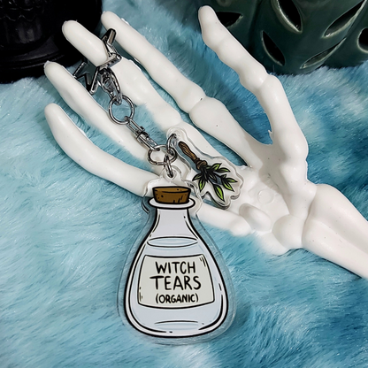 Acrylic keychain with 'Witch Tears (Organic)' whimsical bottle design on a blue textured background.