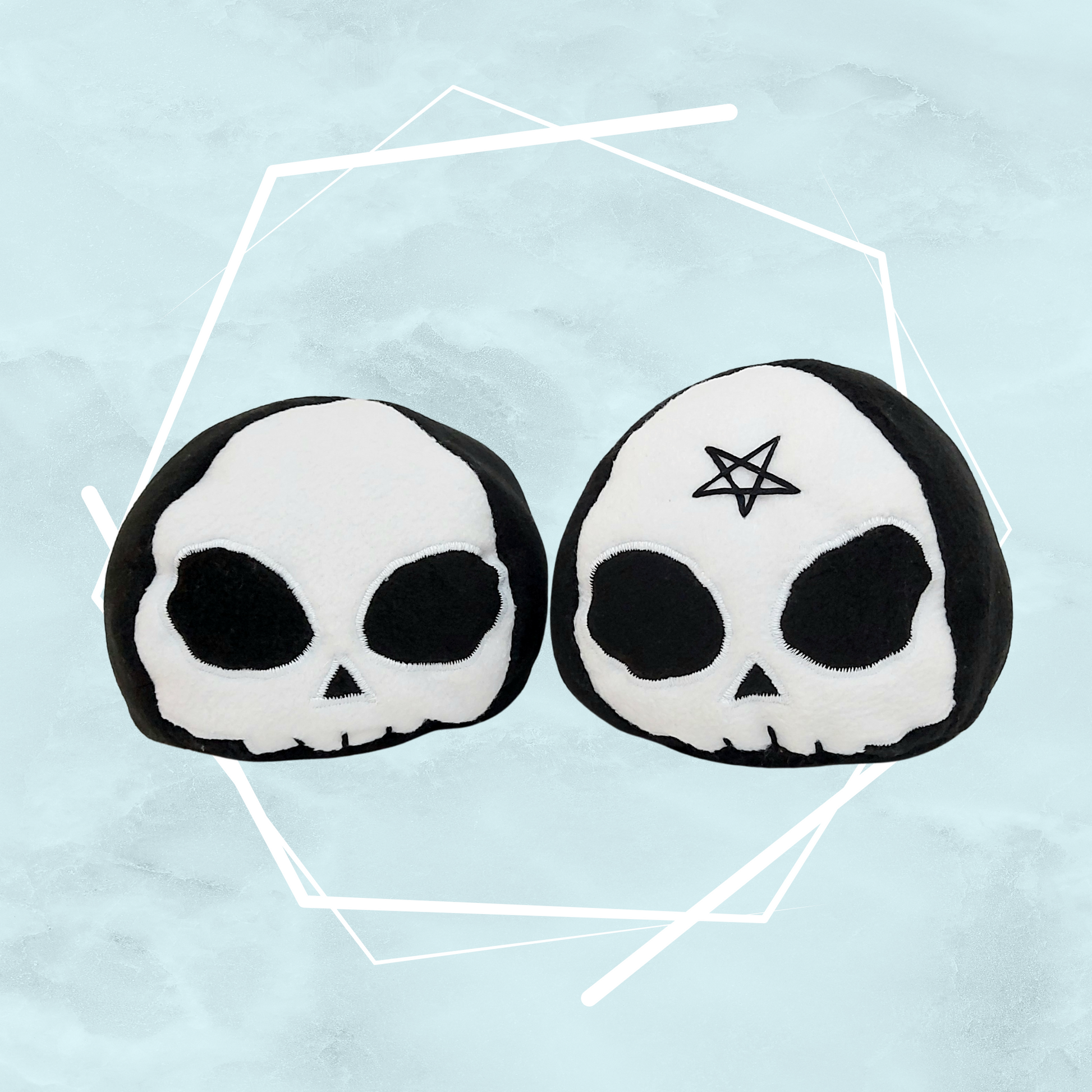 Small quirky plushie toys shaped like skulls with black and white witchy design, one with a pentagram on the forehead.